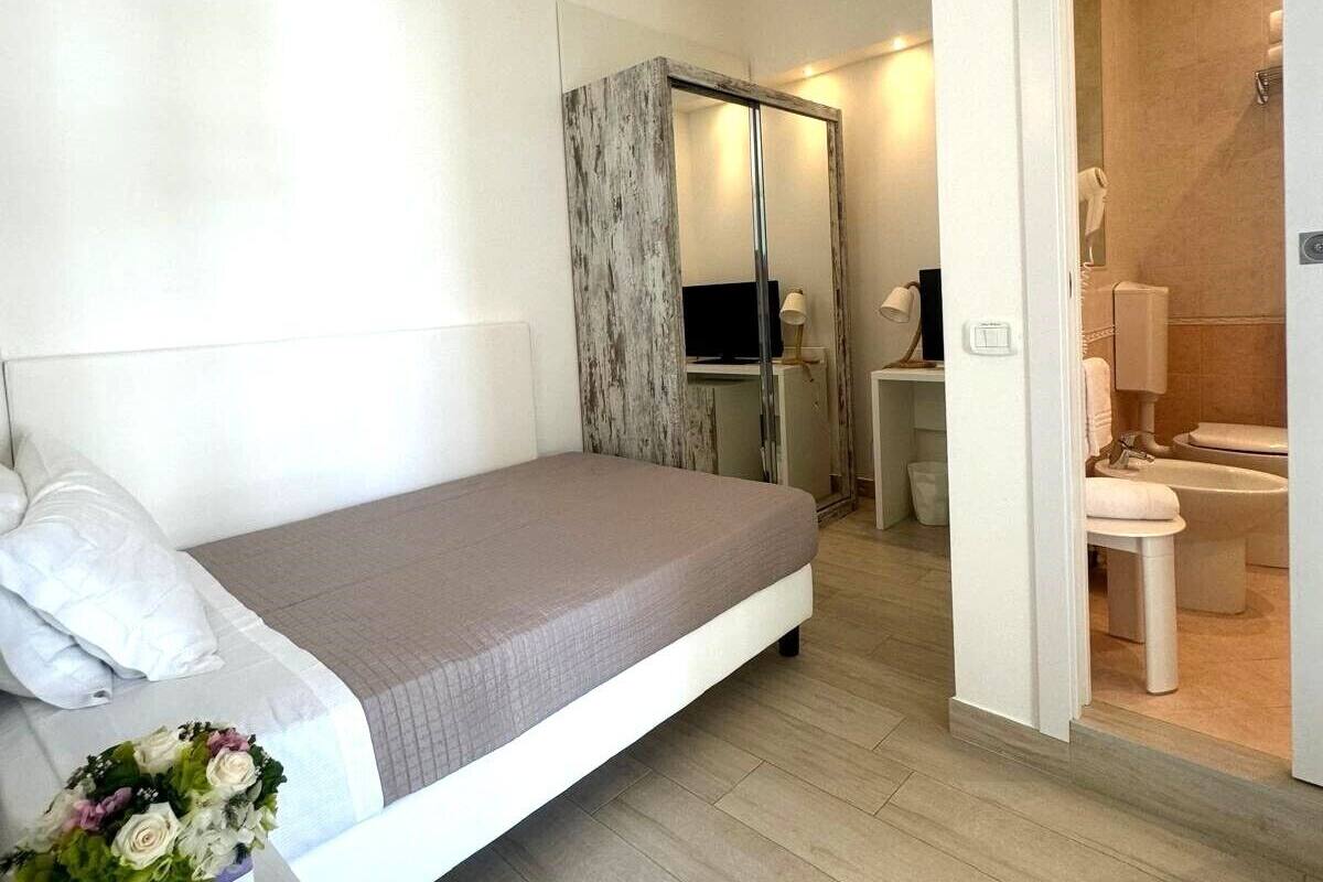 A modern bedroom with a single bed, a small desk, a chair, and a bathroom visible through an open door.
