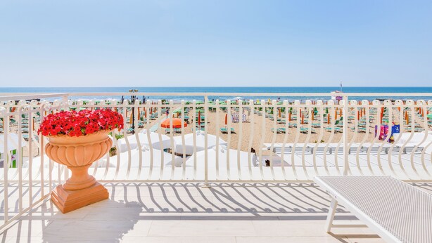 A beach view from a balcony with a potted plant, beach umbrellas, and sun loungers. - Hotel Bellariva (Jesolo)