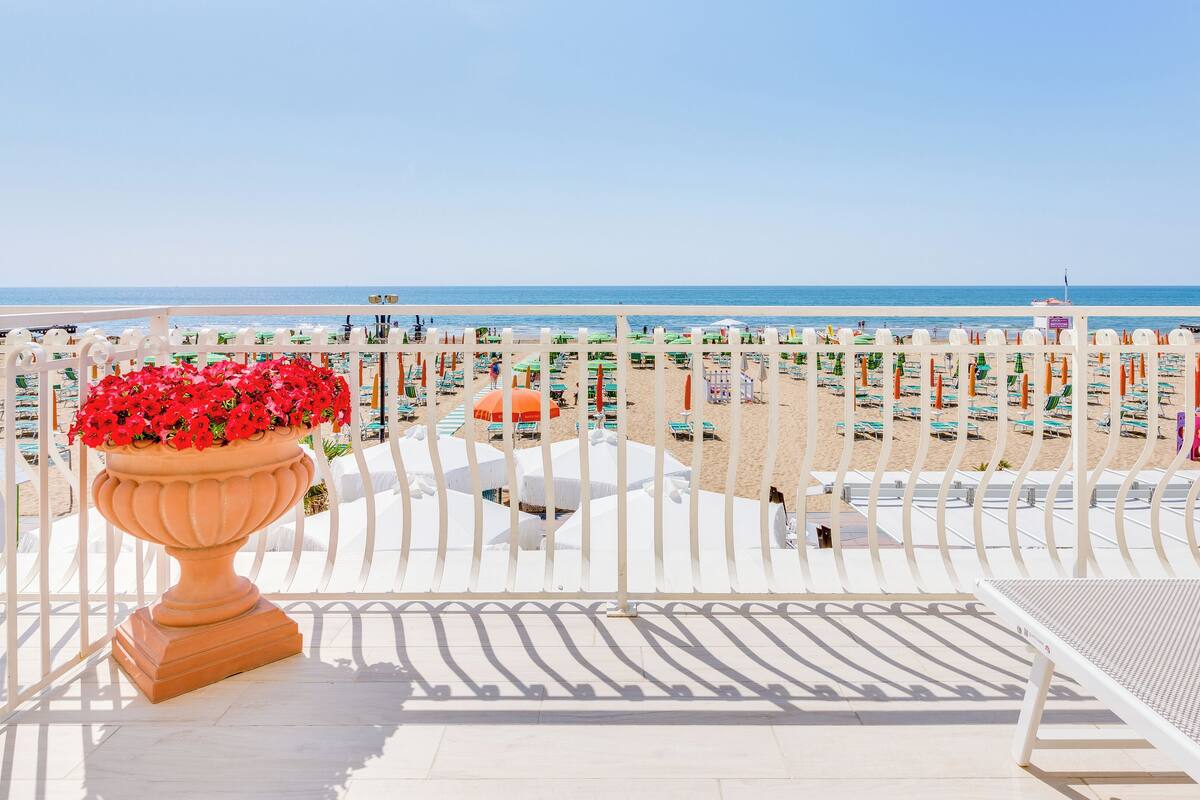 A beach view from a balcony with a potted plant, beach umbrellas, and sun loungers.