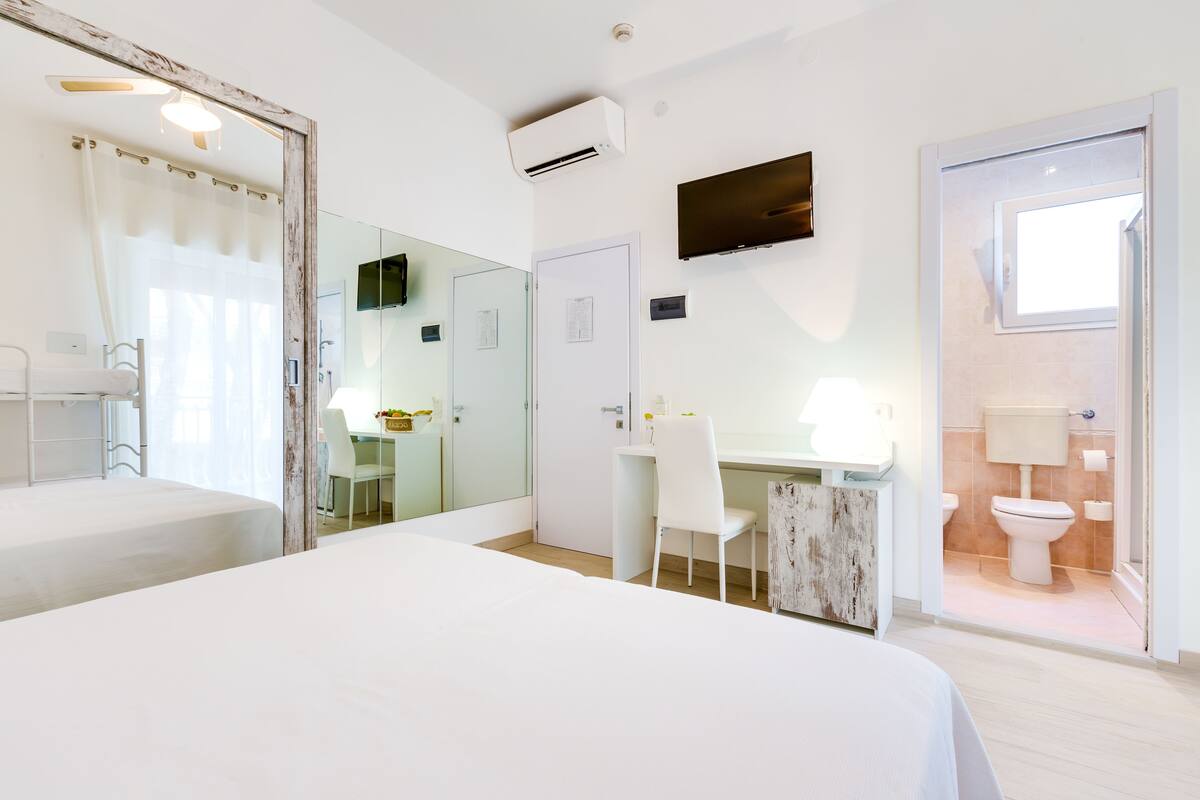 A modern hotel room with a bed, a desk, a chair, a TV, and a bathroom.
