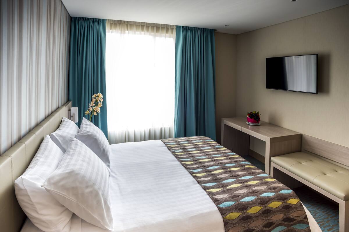 Una habitación de hotel con cama, escritorio, banca y televisión en la pared.