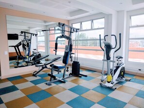 Een sportschool met diverse fitnessapparaten, grote ramen en een geruite vloer.