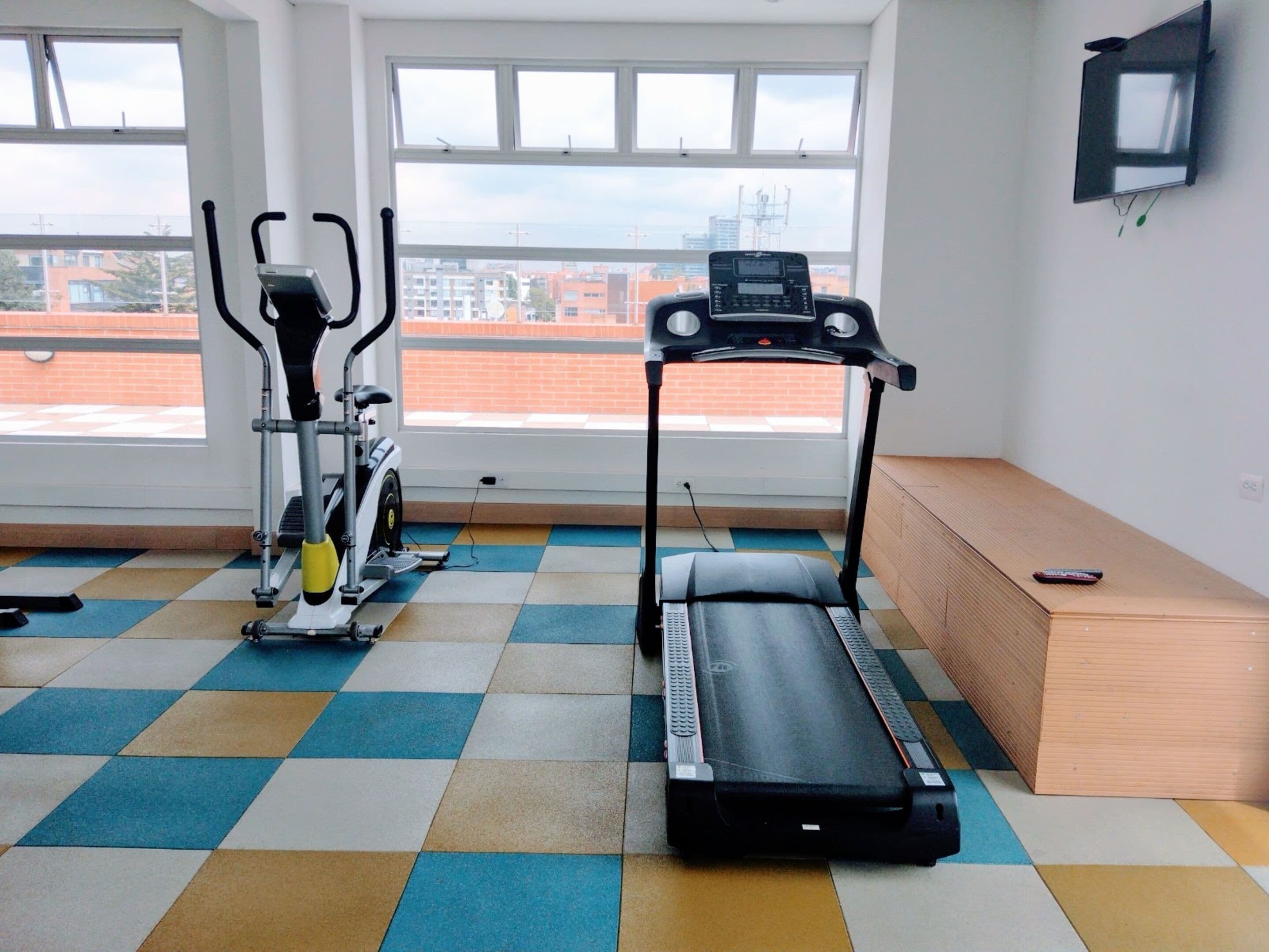 Un gimnasio con una caminadora, una bicicleta estática y un banco.