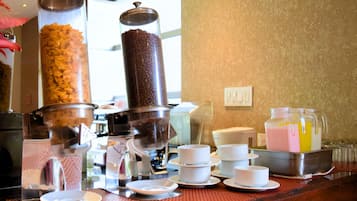 A buffet setup with a coffee machine, a juice dispenser, and various bowls and plates.