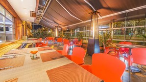 Un restaurant doté d’une terrasse, de chaises rouges et de tables avec des sets de table.