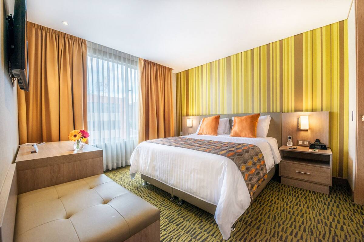 Una habitación de hotel con cama, mesitas de noche, un escritorio, una silla y un televisor.