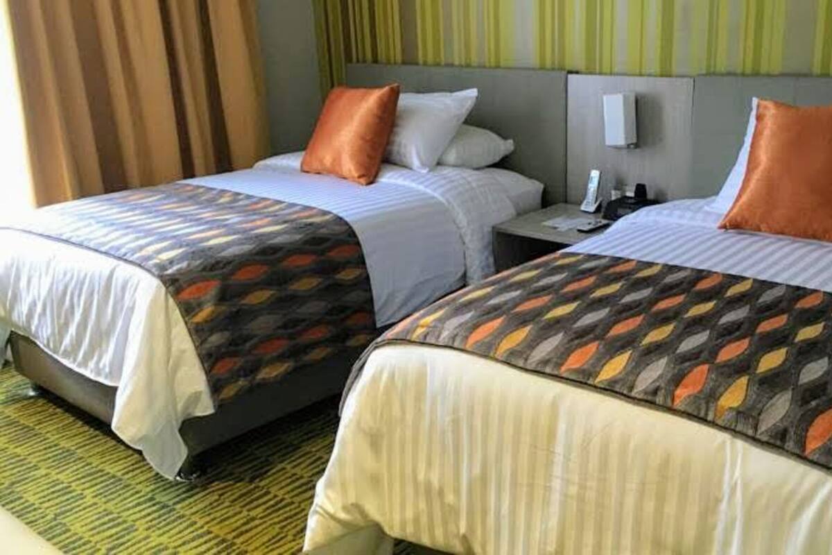 Dos camas dobles con cubrecamas estampadas, una mesita de noche con teléfono y una cortina a rayas.