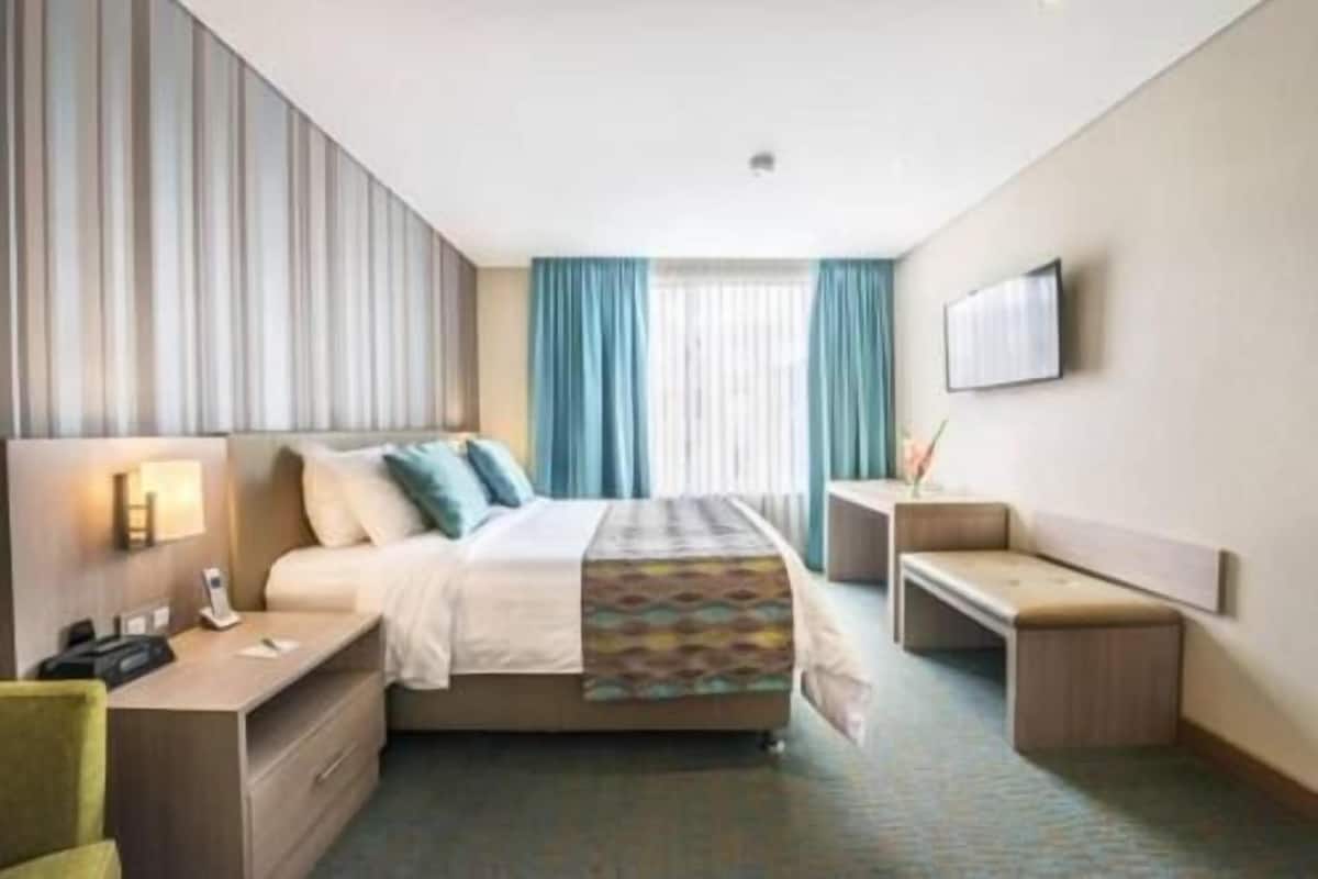 Una habitación de hotel con cama, mesita de noche, escritorio, silla y televisor en la pared.