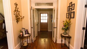 A hallway with wooden flooring, a rug, a door with a window, and a vase with flowers on a side table.