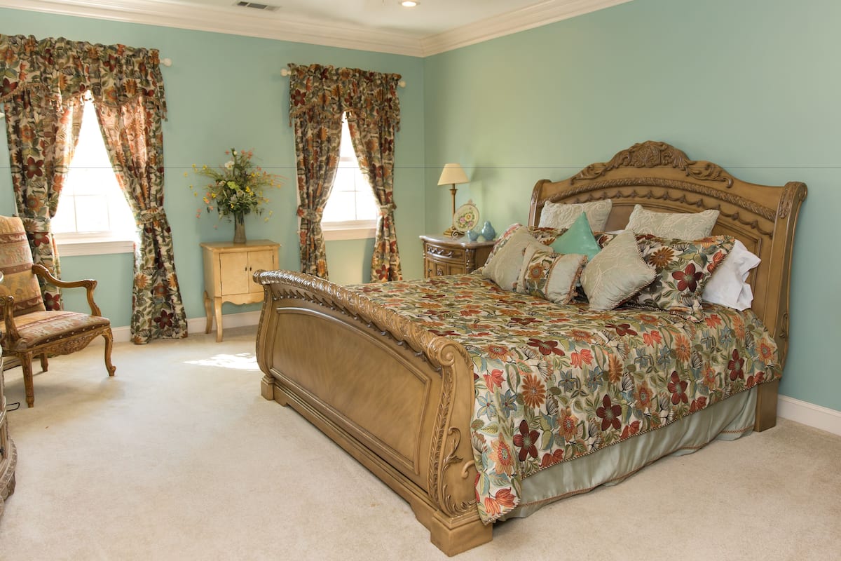 A bedroom with a floral bedspread, a wooden headboard, and a chair.