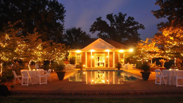 A well-lit outdoor area with a pool, surrounded by trees and tables with chairs, suggesting a dining or event space.