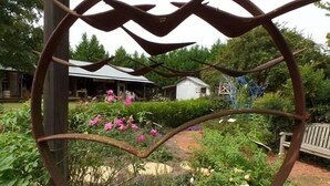 A heart-shaped metal sculpture in a garden with a house and a shed in the background.