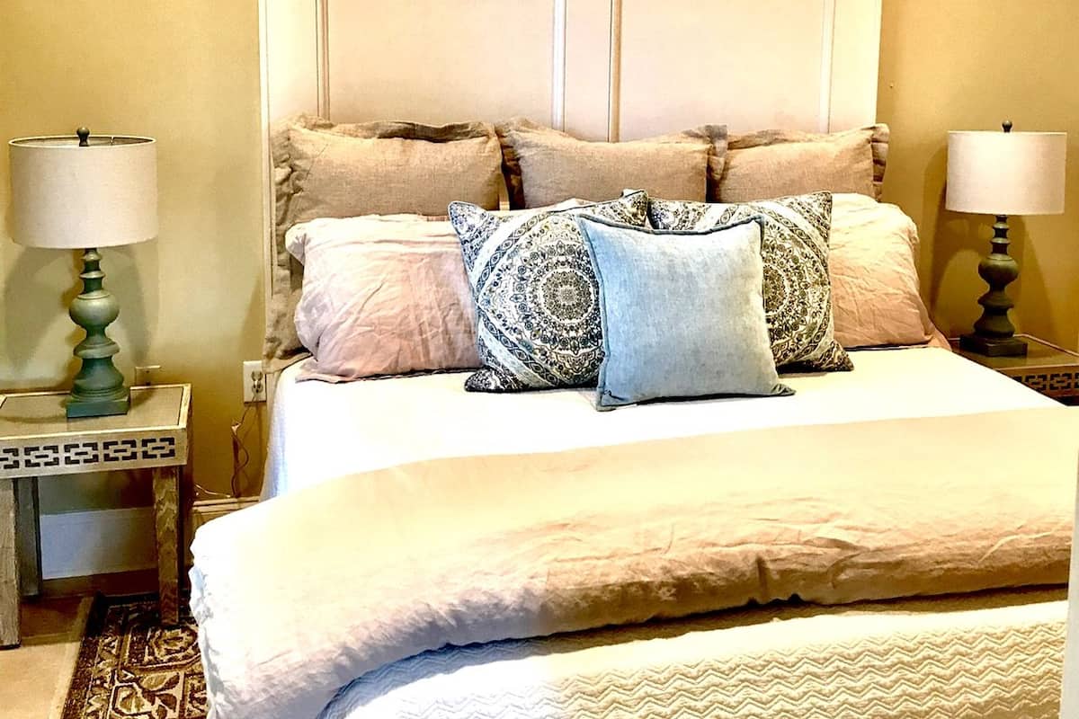A neatly made bed with multiple pillows and a headboard, flanked by two bedside tables with lamps.