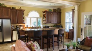 A kitchen with dark wooden cabinets, a central island with bar stools, a refrigerator, and a dining area with a sofa and chairs.