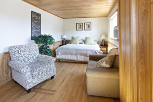 A cozy room with a bed, two nightstands, a lamp, a patterned armchair, a sofa, and a decorative wall piece.