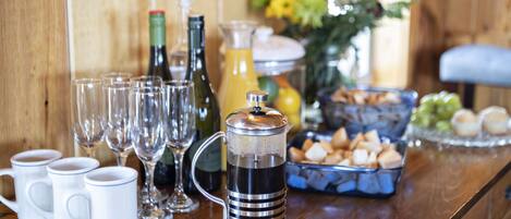 Una encimera de cocina con una cafetera, botellas de vino, vasos y un frutero.