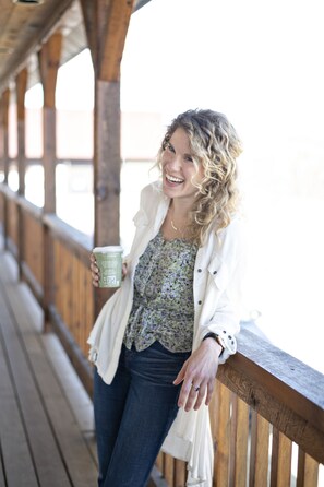 A person standing on a wooden deck with a railing, holding a cup.