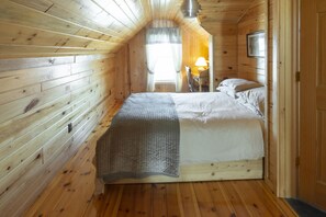 A cozy wooden cabin bedroom with a single bed, a nightstand, and a window with curtains.