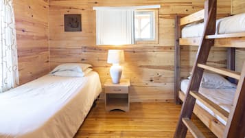 A wooden cabin room with bunk beds, a bedside table with a lamp, and a window with blinds.