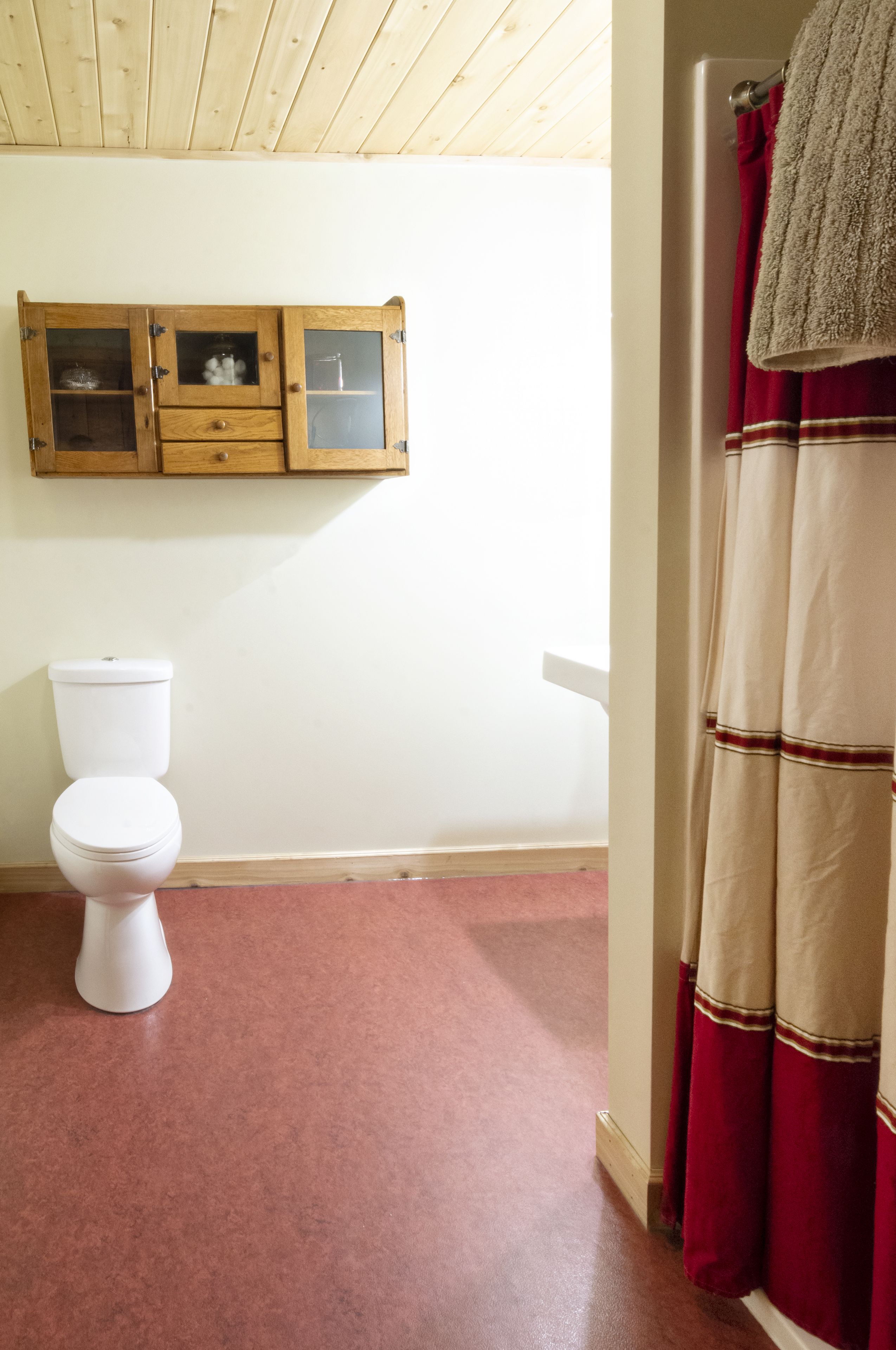 A bathroom with a white toilet, wooden cabinets, and a red and beige shower curtain.