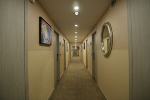 Un pasillo largo y estrecho de hotel con puertas a ambos lados, iluminación empotrada y una obra enmarcada en la pared izquierda.