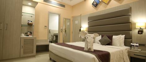 Una habitación de hotel moderna con una cama grande, un armario, una tocador con espejo y una mesita de noche con lámpara.