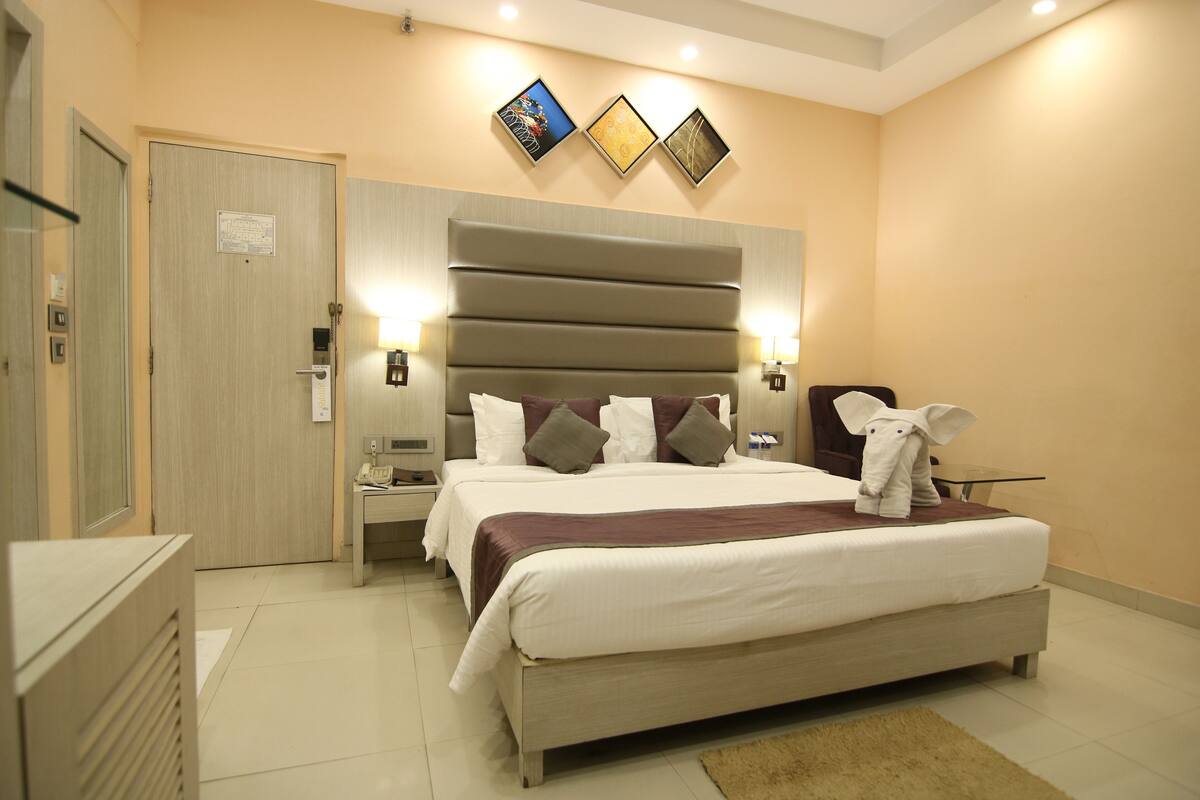Une chambre d’hôtel avec un grand lit, des tables de chevet, une commode, une porte et une œuvre d’art accrochée au mur.