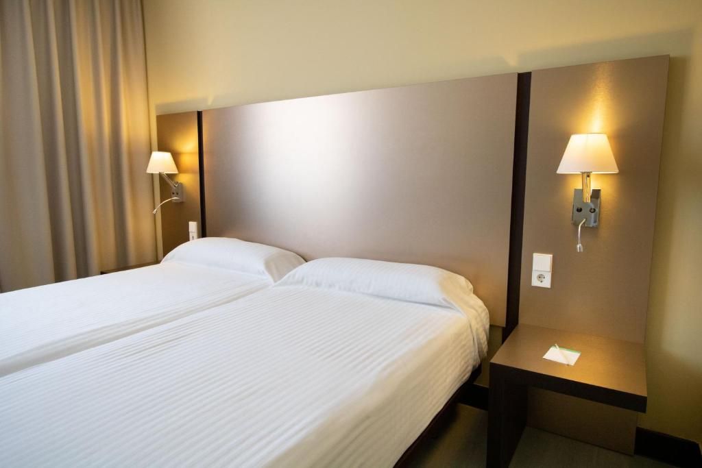 Habitación de hotel con cama doble, dos lámparas de noche, una mesita de noche y una cortina.