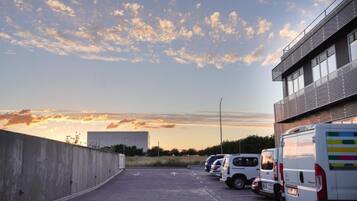 Un estacionamiento con varios vehículos, un muro de concreto y un edificio con fachada metálica.