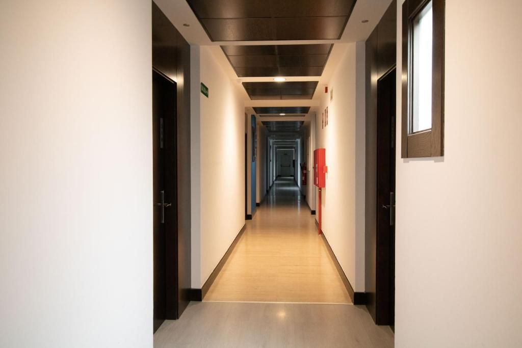 Ein Hotelkorridor mit Türen auf beiden Seiten, einem Feuerlöscher an der rechten Wand und einer Decke mit eingelassener Beleuchtung.