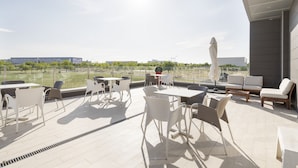 A rooftop terrace with outdoor seating, a view of the city, and a modern building in the background. - Hotel Route 42 (Illescas)