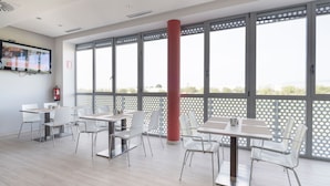 A modern dining area with large windows, white chairs, and tables. - Hotel Route 42 (Illescas)