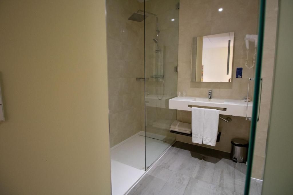 Un baño moderno con ducha de vidrio, lavamanos blanco y espejo.