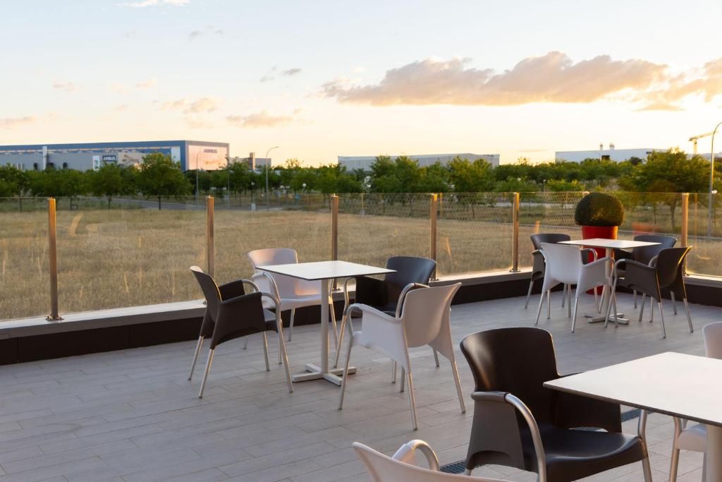 An outdoor seating area with tables and chairs, overlooking a field and industrial buildings.