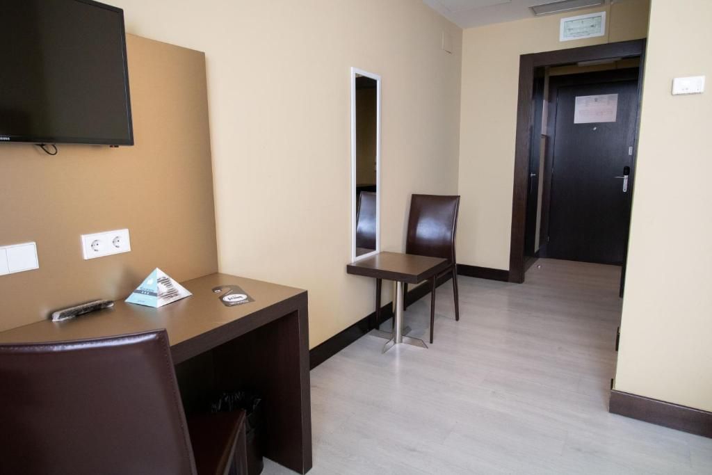 Une chambre d’hôtel équipée d’un bureau, d’une chaise, d’un téléviseur fixé au mur et d’une porte avec une pancarte.