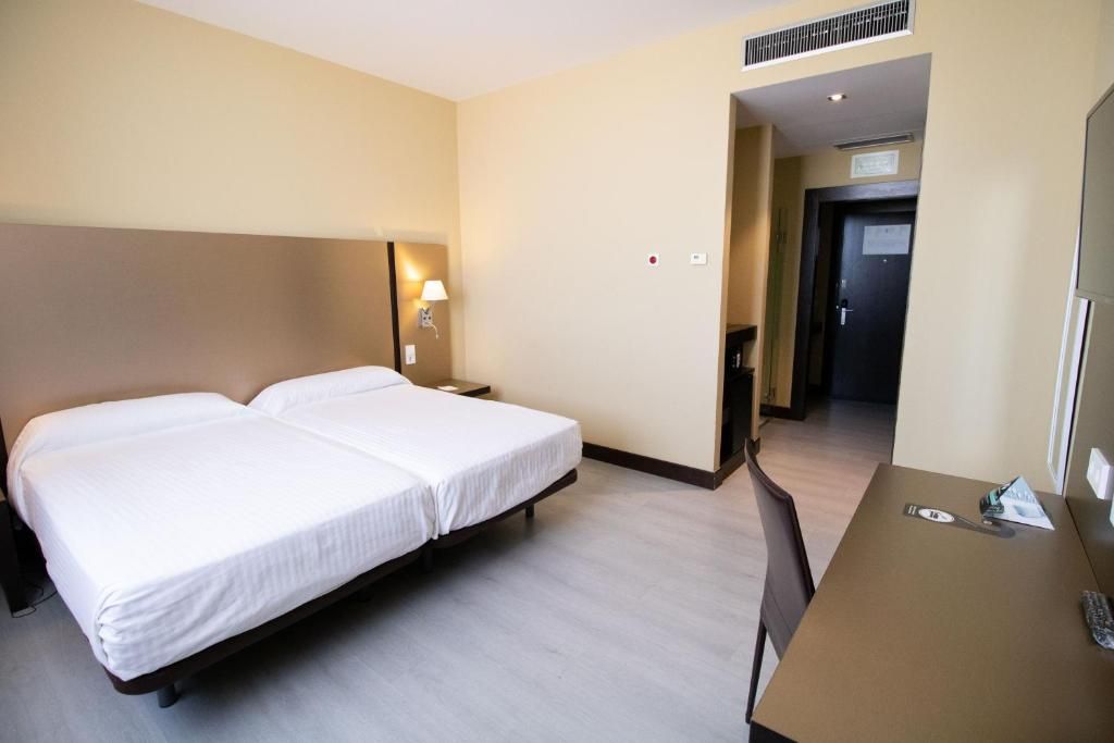 Habitació d'hotel amb dos llits, un escriptori i una cadira.