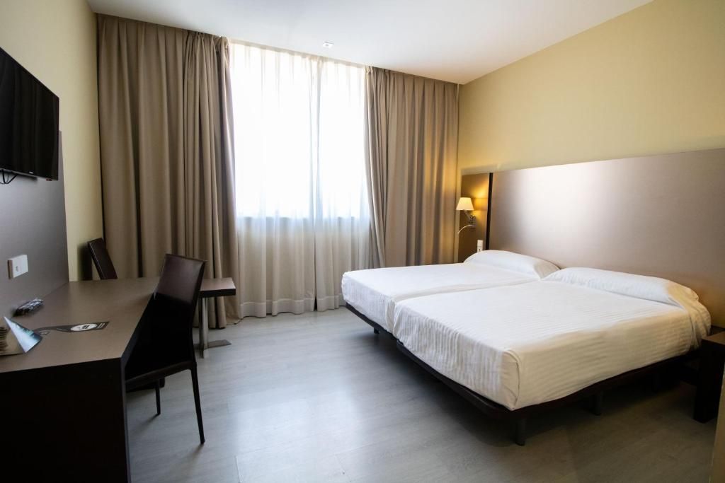 A hotel room with a bed, a desk, a chair, a TV, and curtains.