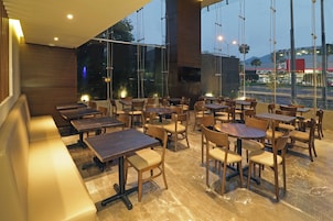 Un interior de restaurante con diversas opciones de asientos, incluyendo mesas y cabinas, amplias ventanas que ofrecen vistas al exterior, y un diseño moderno con mobiliario de madera.