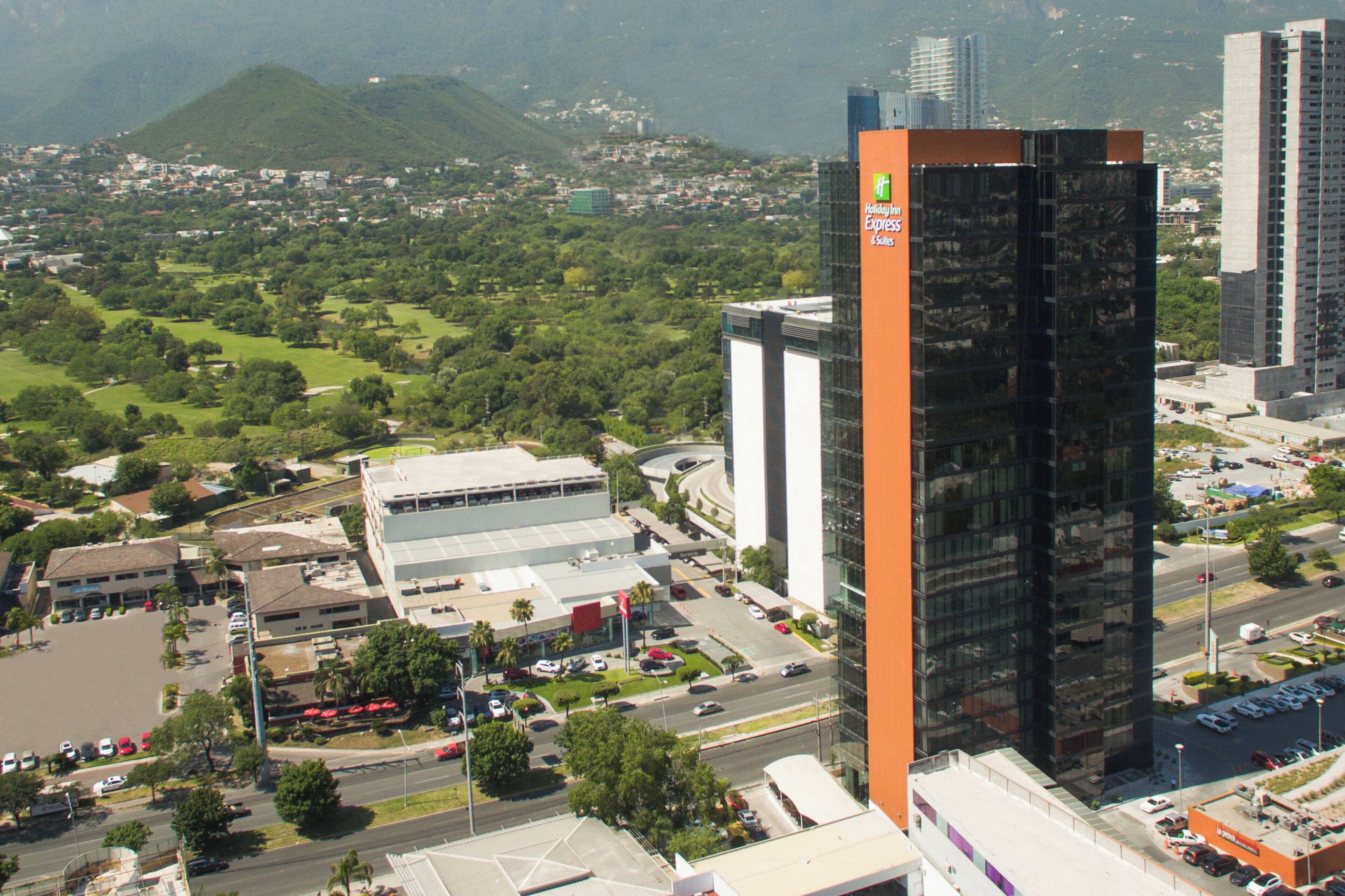 A high-rise building with a prominent orange facade, surrounded by a cityscape with greenery and other buildings.