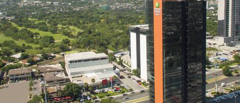A high-rise building with a prominent orange facade, surrounded by a cityscape with greenery and other buildings.