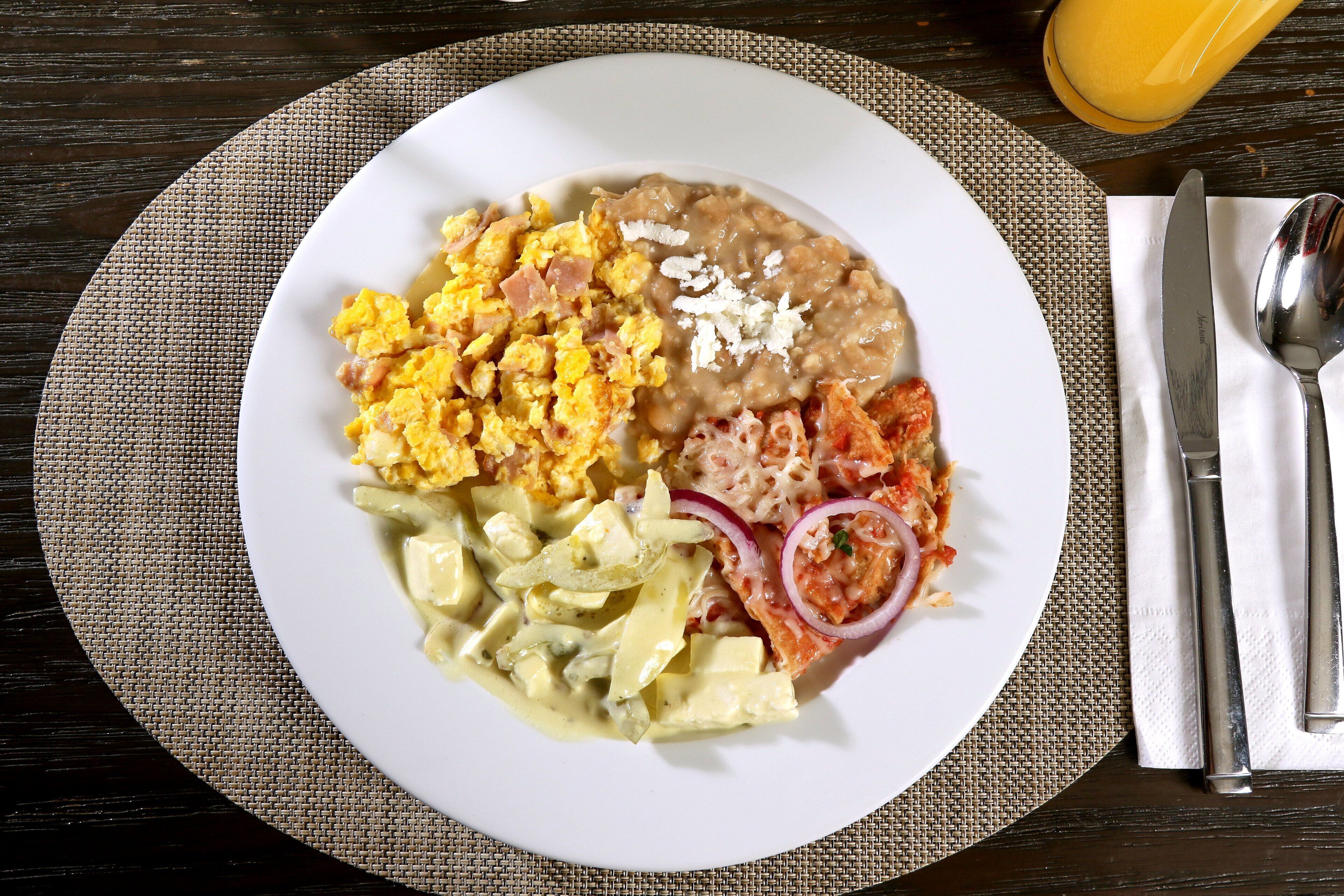 Un plato de huevos revueltos, frijoles refritos y una ensalada con cebollas y queso sobre un plato blanco.