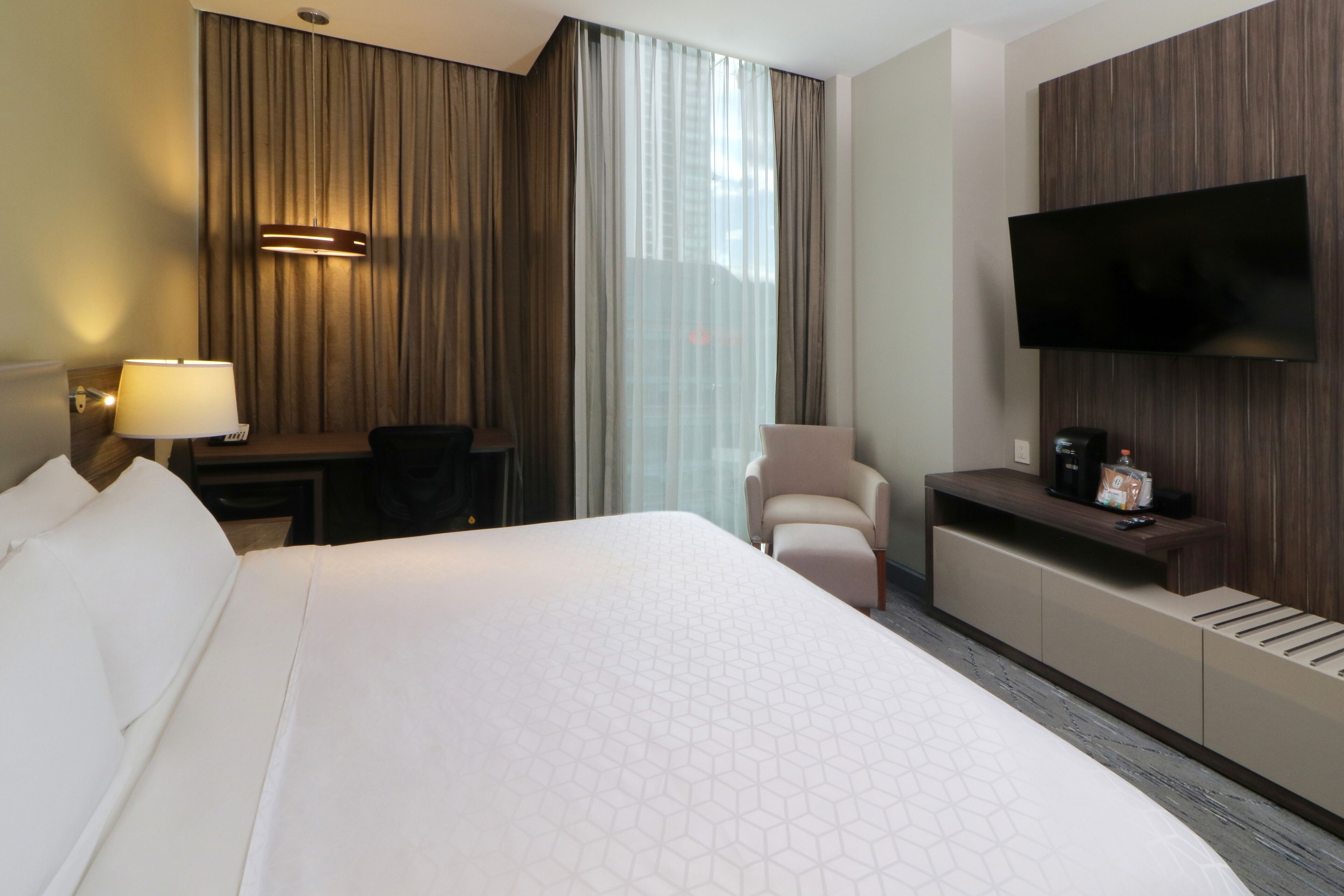 Quarto de hotel com uma cama grande, uma escrivaninha, uma cadeira, uma televisão e um minibar.