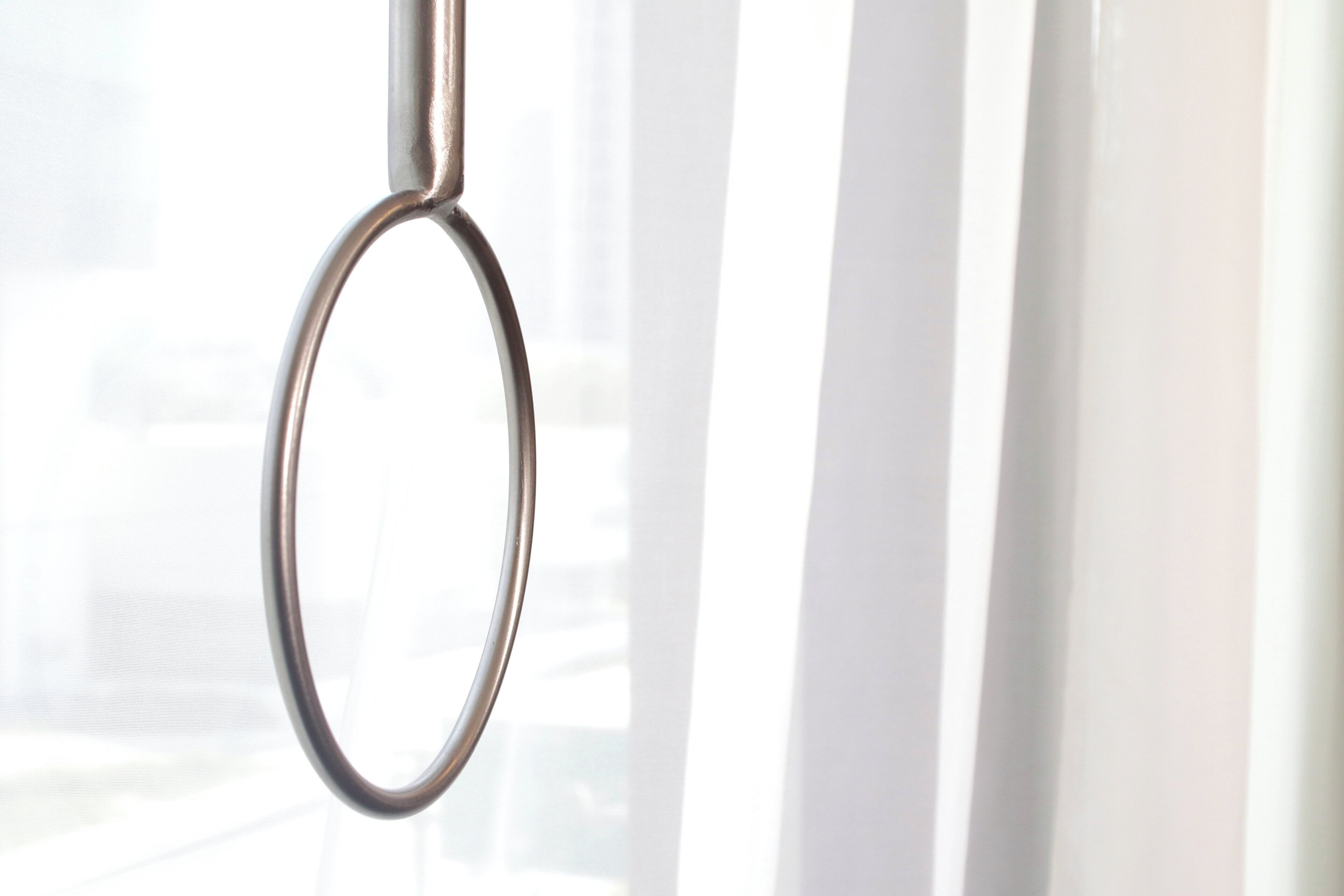 A metal ring attached to a vertical structure, likely a window handle, with a blurred background suggesting an urban setting.