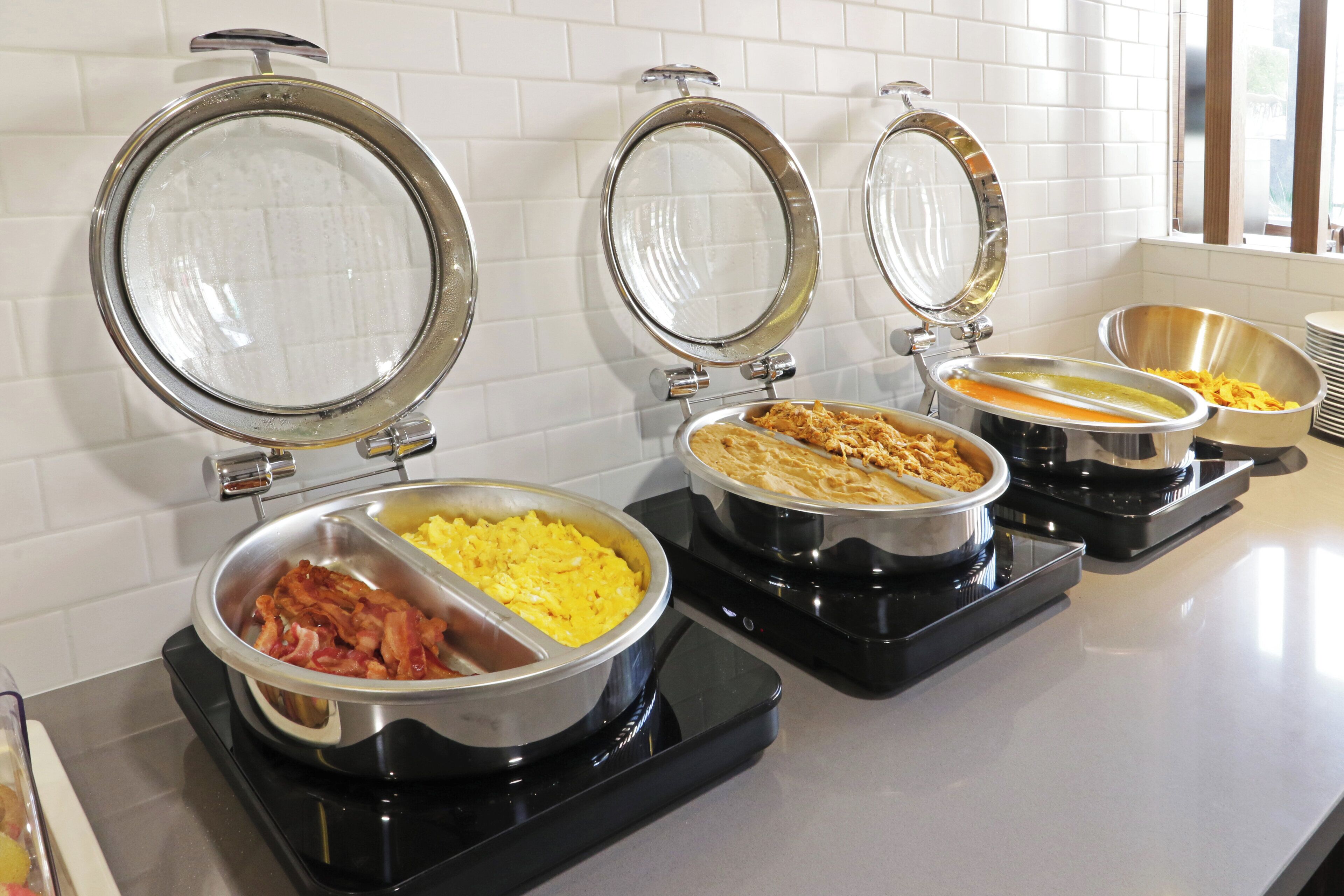 Ein Buffet mit verschiedenen Speisen in Metallbehältern, darunter Rührei und Speck.