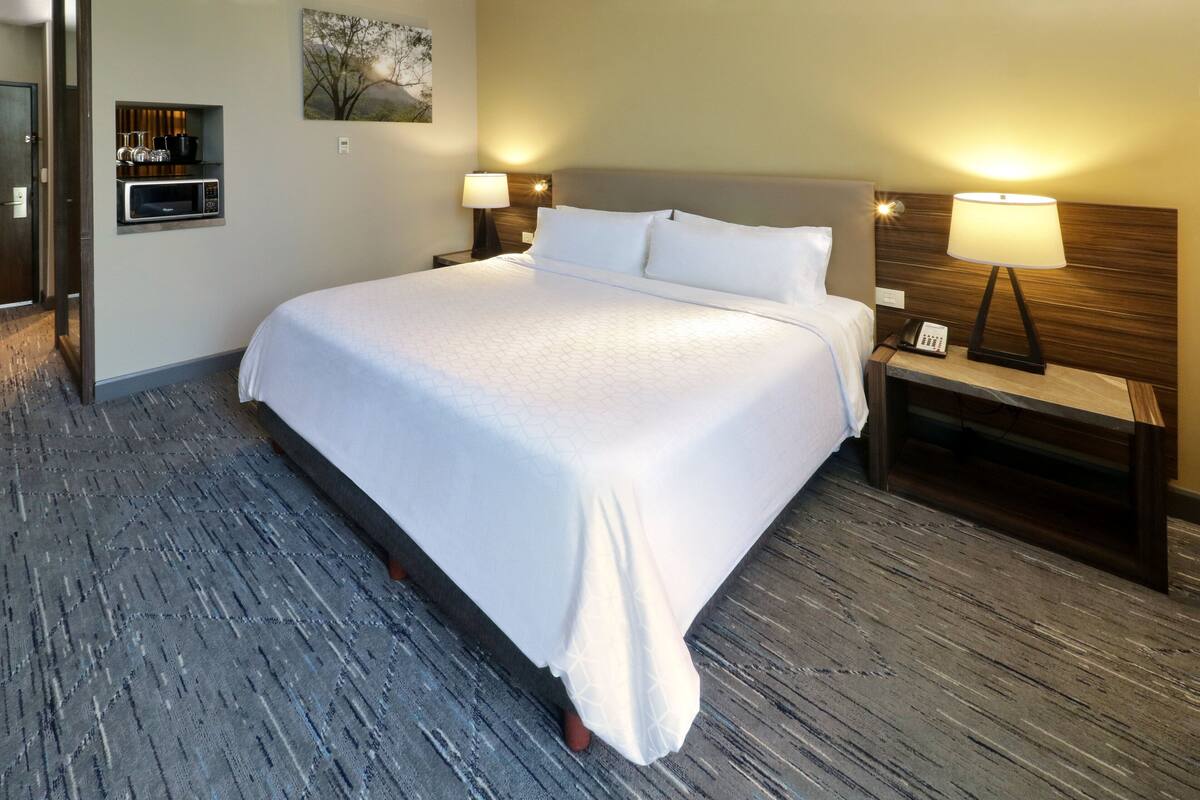 A hotel room with a large bed, bedside lamps, a microwave, and a small shelf with glasses.