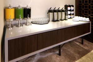 A hotel reception area with a long counter, beverage dispensers, and coffee machines. - Holiday Inn Express & Suites Monterrey Valle by IHG (San Pedro Garza García)