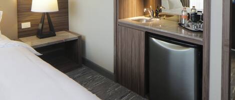 A hotel room with a bed, a bedside table with a lamp, a built-in sink, and a compact dishwasher.