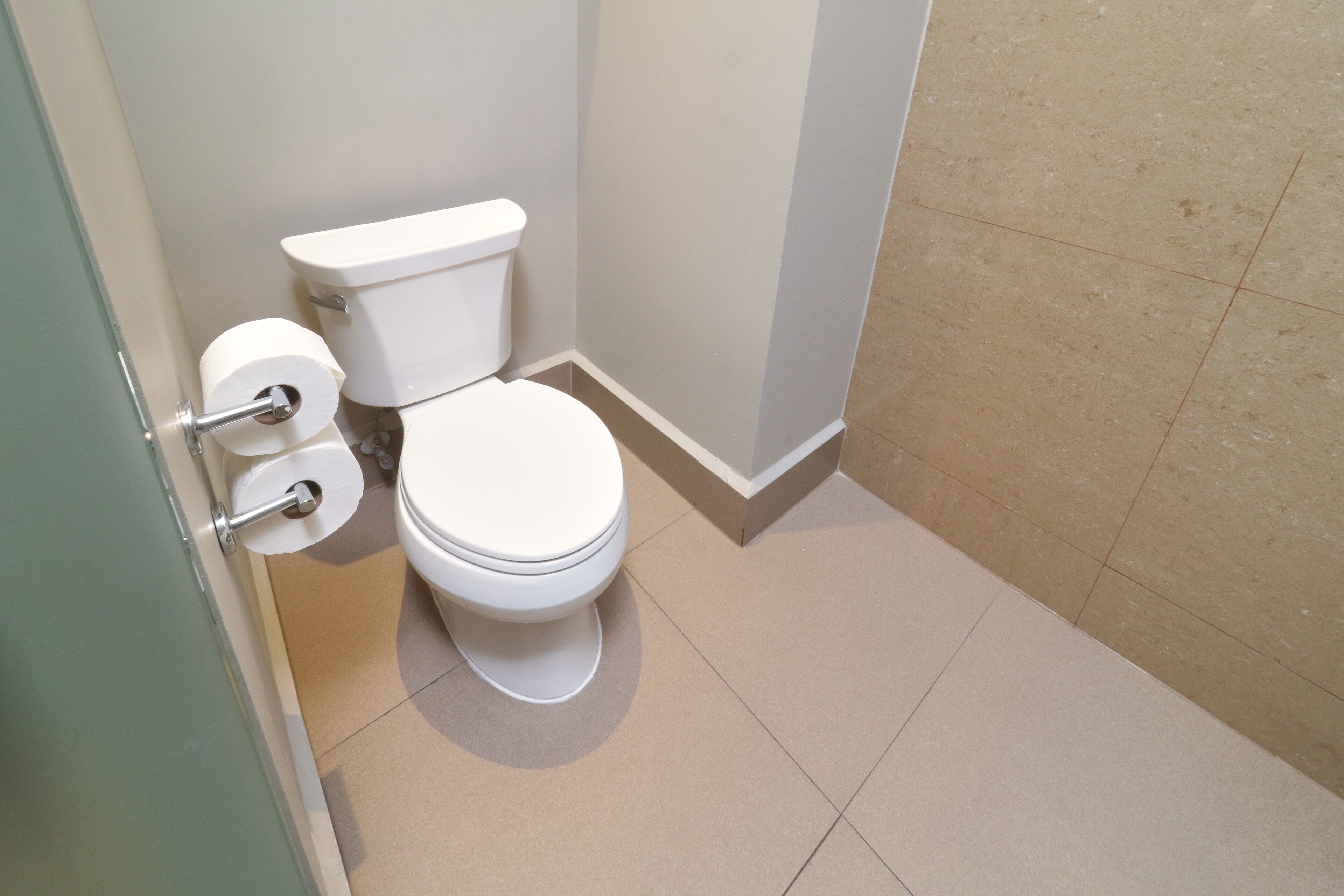 A bathroom with a white toilet, a toilet paper holder, and a tiled floor.