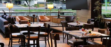 Un restaurante con una decoración moderna, que cuenta con asientos de cuero, mesas de madera y una gran pantalla de televisión en la pared.