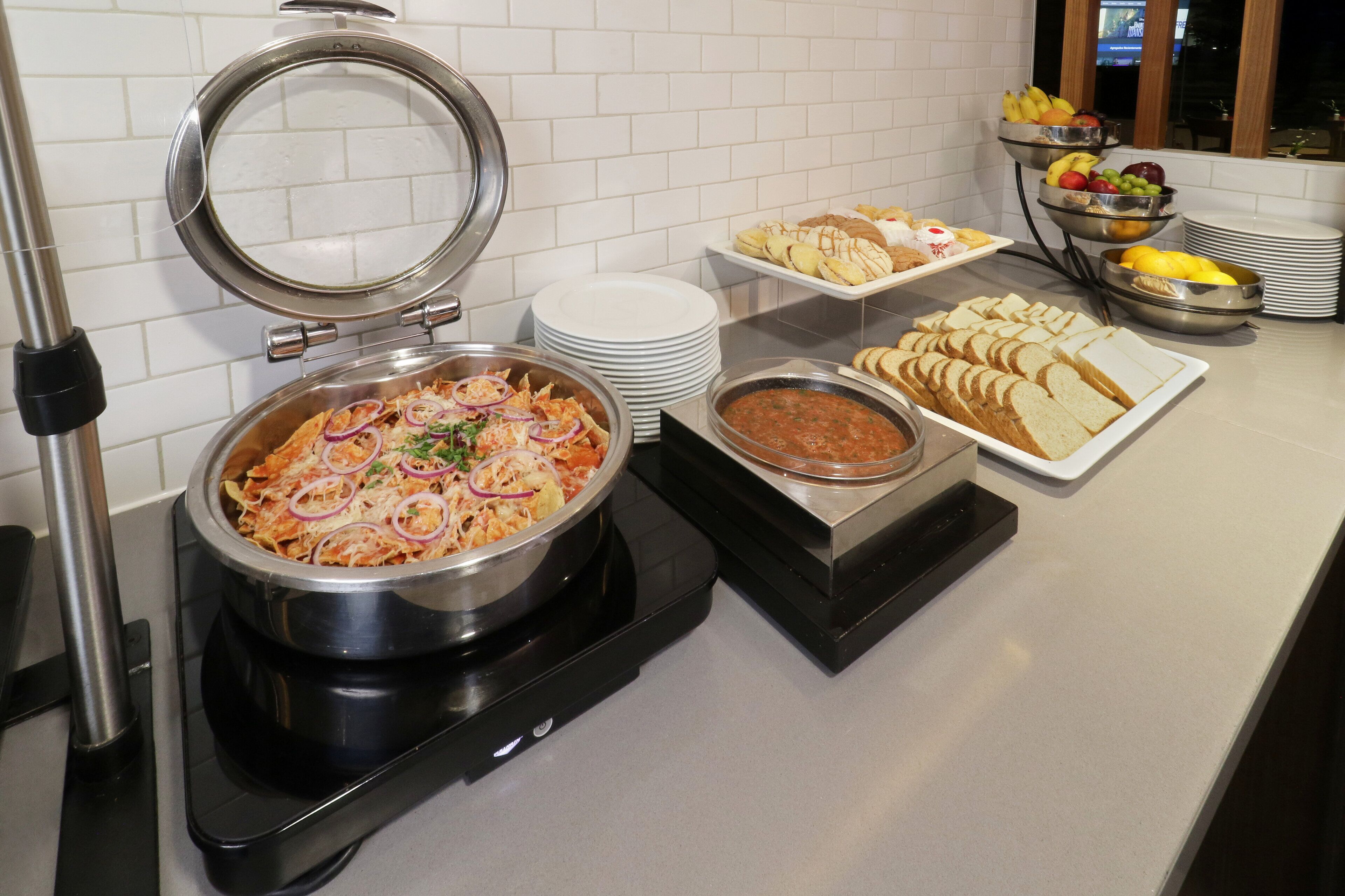 Disposición de bufé con diversos platos, incluyendo una olla grande de comida, pan y cuencos de fruta.